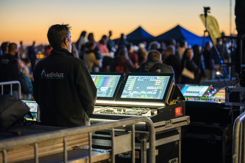 Technician managing sound and lighting panels during an outdoor event at sunset.